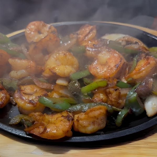 Sizzling shrimp fajitas with green peppers and onions on a black skillet, emitting steam.