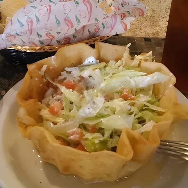 A taco salad in a crispy fried tortilla bowl with lettuce, tomatoes, and dressing.
