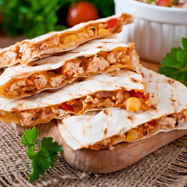 Stacked chicken and cheese quesadillas with corn and peppers, garnished with parsley on a wooden board.